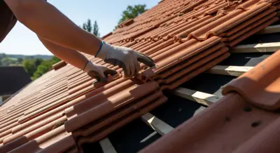 Gloved hands arranging terracotta roof tiles on a sunlit pitched roof, with a pile of tiles nearby.