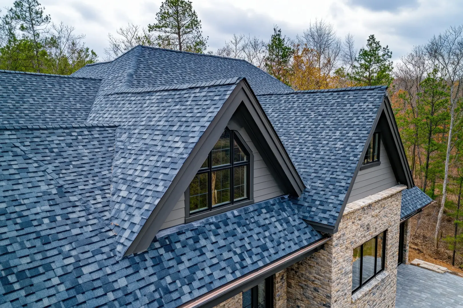 Blue slate roof with gabled dormers and a stone exterior on a wooded hillside house.