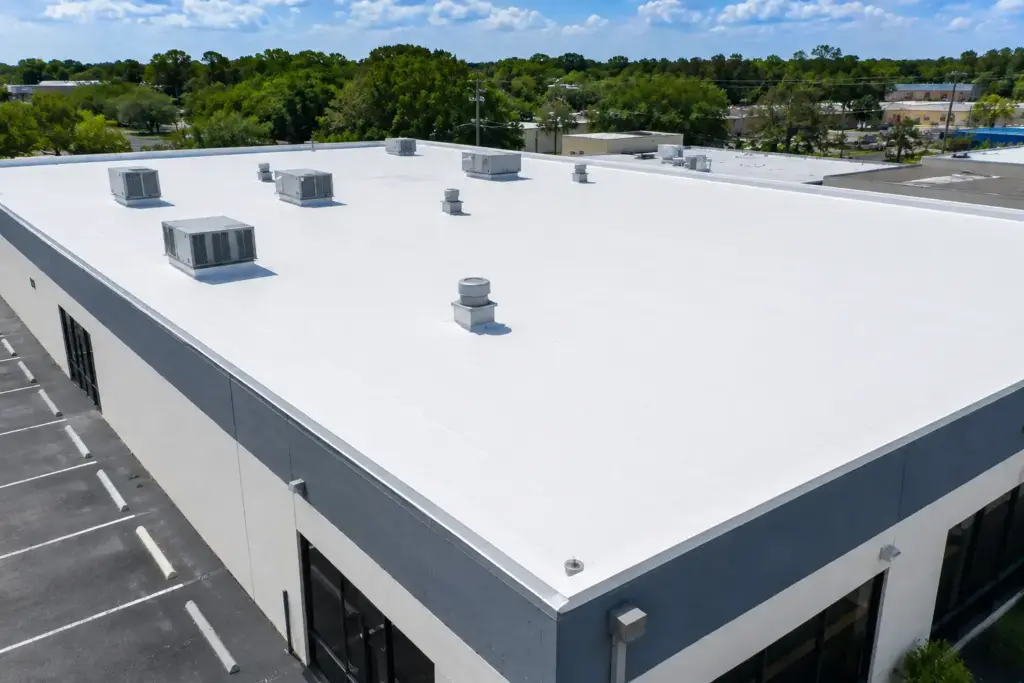 White flat-roofed commercial building with several HVAC units and vents; surrounding parking lot visible nearby.